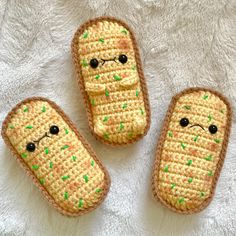 three crocheted hot dogs with green sprinkles on them sitting on a white surface