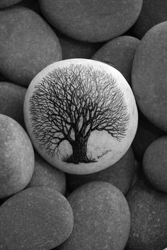 a rock with a tree painted on it surrounded by large, round rocks and gravel