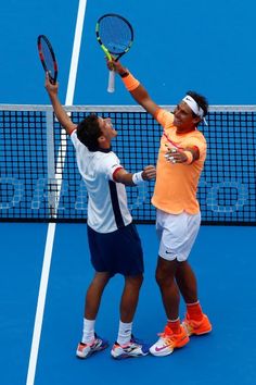 two tennis players giving each other high fives on the court with their racquets raised