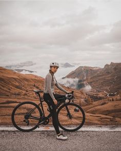 a person riding a bike on the side of a road with mountains in the background