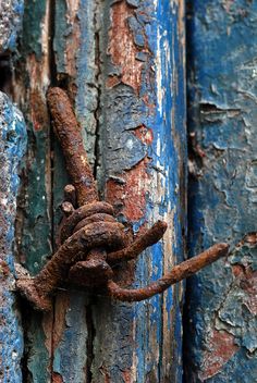 an old rusted metal hook on the side of a blue wooden door with peeling paint