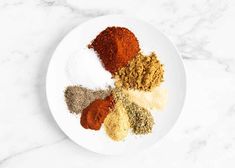 spices on a white plate sitting on a marble counter top, with one seasoning mix in the middle