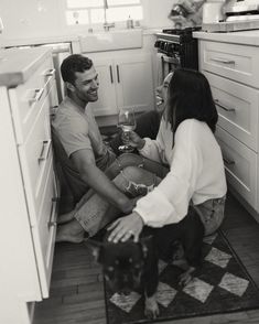 a man and woman sitting on the kitchen floor with a dog in front of them