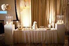 a table topped with lots of cakes and desserts next to a window covered in curtains