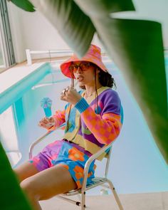 a woman sitting in a chair next to a pool wearing a colorful outfit and hat