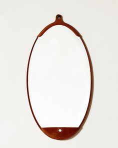 an oval mirror hanging on the wall with a wooden frame and leather strap around it