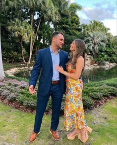 a man and woman standing next to each other in front of a pond with palm trees