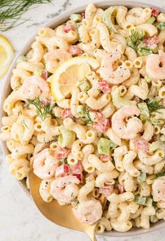 a bowl full of pasta salad with lemon wedges and dill on the side