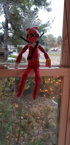 a red stuffed animal hanging from the side of a window sill in front of a tree