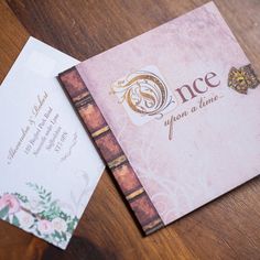 two wedding cards sitting on top of a table next to an envelope with the word once upon it