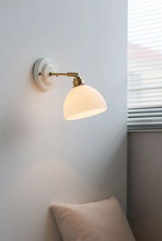 a white wall mounted light next to a window in a room with a beige couch