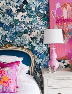 a pink lamp sitting on top of a white table next to a blue and pink bed