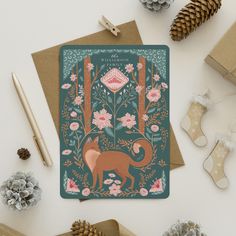 a card with an image of a fox surrounded by flowers and pine cones on the table