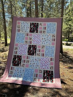 a patchwork quilt hanging on a clothes line in the woods with trees behind it