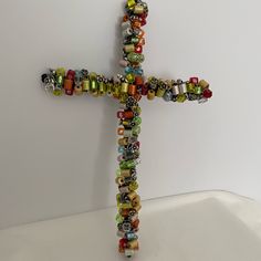 a multicolored beaded cross hanging on the wall in front of a white background