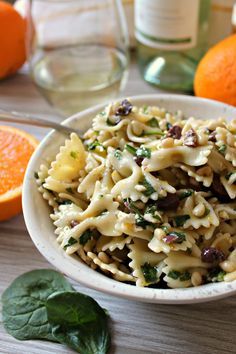 a white bowl filled with pasta and spinach next to oranges on a table