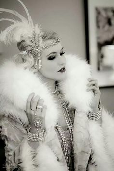 a woman in a white feathered coat and headpiece holding her hand up to her face