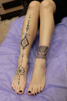 a woman's legs with tattoos on them sitting on a purple bed coverlet