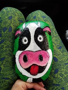 a hand holding a painted rock with a cow's face and tongue on it