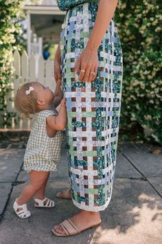 a woman holding the hand of a toddler who is touching her leg with both hands