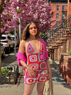 a woman is standing on the sidewalk with her hand in her pockets and wearing a colorful crocheted dress