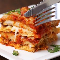 a fork is stuck into some lasagna casserole on a white plate