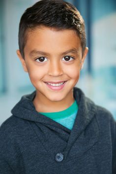 a young boy smiling at the camera with his hair pulled back and wearing a hoodie