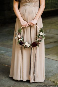 a woman in a long dress is holding a flower wreath and wearing a ring on her finger