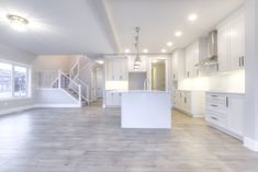 an empty kitchen and living room in a new home with white cabinets, counter tops, and stairs