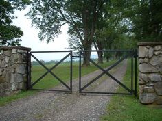 an iron gate and stone wall leading to a grassy field with trees in the background