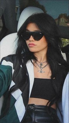 a woman wearing sunglasses sitting in the back of a car with her hand on her hip