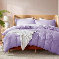 a bed with purple comforter and pillows in a pink room next to a potted plant