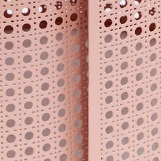 a close up view of the perfored surface on a pink wall with holes in it