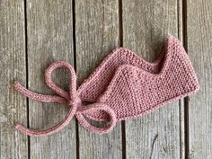 a crocheted pink hat is laying on a wooden surface with a knot at the end