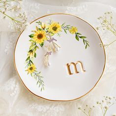 a white plate with yellow flowers and the letter m on it is surrounded by daisies