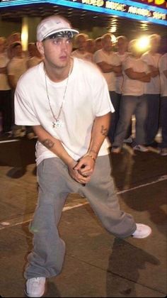 a man in white shirt and grey pants doing tricks on a skateboard with other people behind him