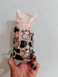 a hand holding up a glass with a cow pattern on it and tissue paper wrapped around the bottom