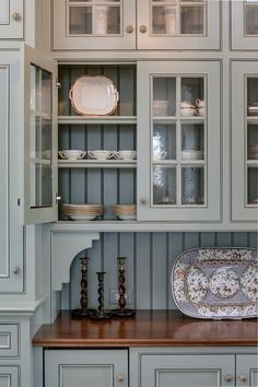 a kitchen with gray cabinets and wooden counter tops, white dishes on the cupboards