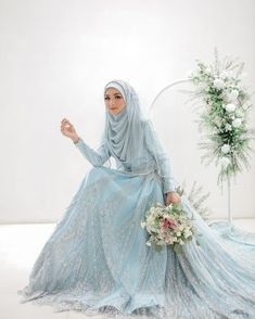 a woman in a blue dress is sitting on the floor and holding a flower bouquet