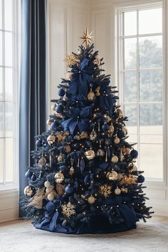 a blue christmas tree with gold and silver ornaments on it in front of a window