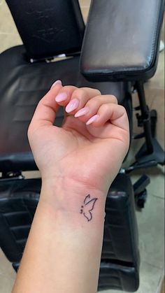 a woman's hand with a small butterfly tattoo on her left wrist, next to a chair