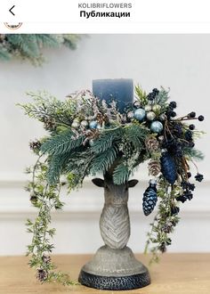 a vase filled with flowers and greenery on top of a wooden table next to a candle