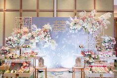 a floral display with flowers on the wall and tables full of desserts in front of it