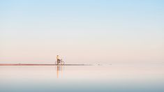 a person riding a bike across a large body of water with the sky in the background