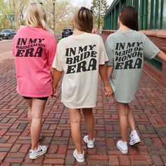 three women in matching shirts are walking down the brick sidewalk holding hands with each other