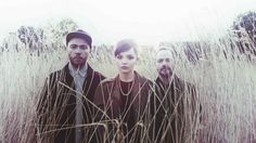 three people standing in tall grass with one person wearing a hat and the other looking at the camera