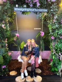 two women sitting on swings in front of a display