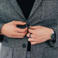 a man in a gray suit with his hands on his lapel and wearing two rings