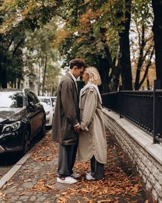 a man and woman standing next to each other in front of cars on the street