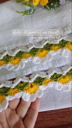 the hand is holding three pieces of crocheted fabric with yellow and green trim